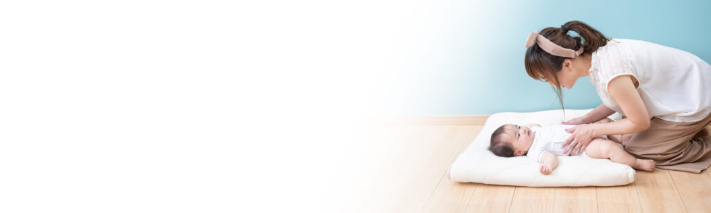 おむつ替えマットの上で赤ちゃんにやさしく語りかける母親の様子。新生児から使えるスキンケアのやさしさと安心感をイメージしたビジュアル。